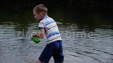 小男孩尖叫着，怒气冲冲地从桶里的水倒进河里。 儿童自然游戏